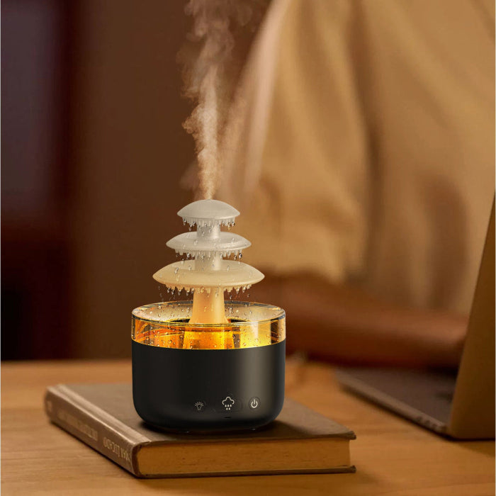 Humidificateur nuage de pluie coloris noir, bassin illuminé en ambré, posé sur un livre à côté d'un ordinateur portable