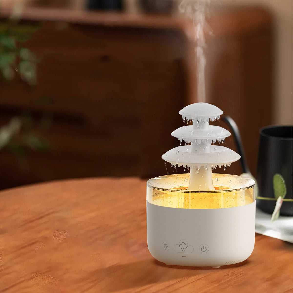 Humidificateur nuage de pluie sur une table en bois clair à côté d'une tasse noire et d'une plante